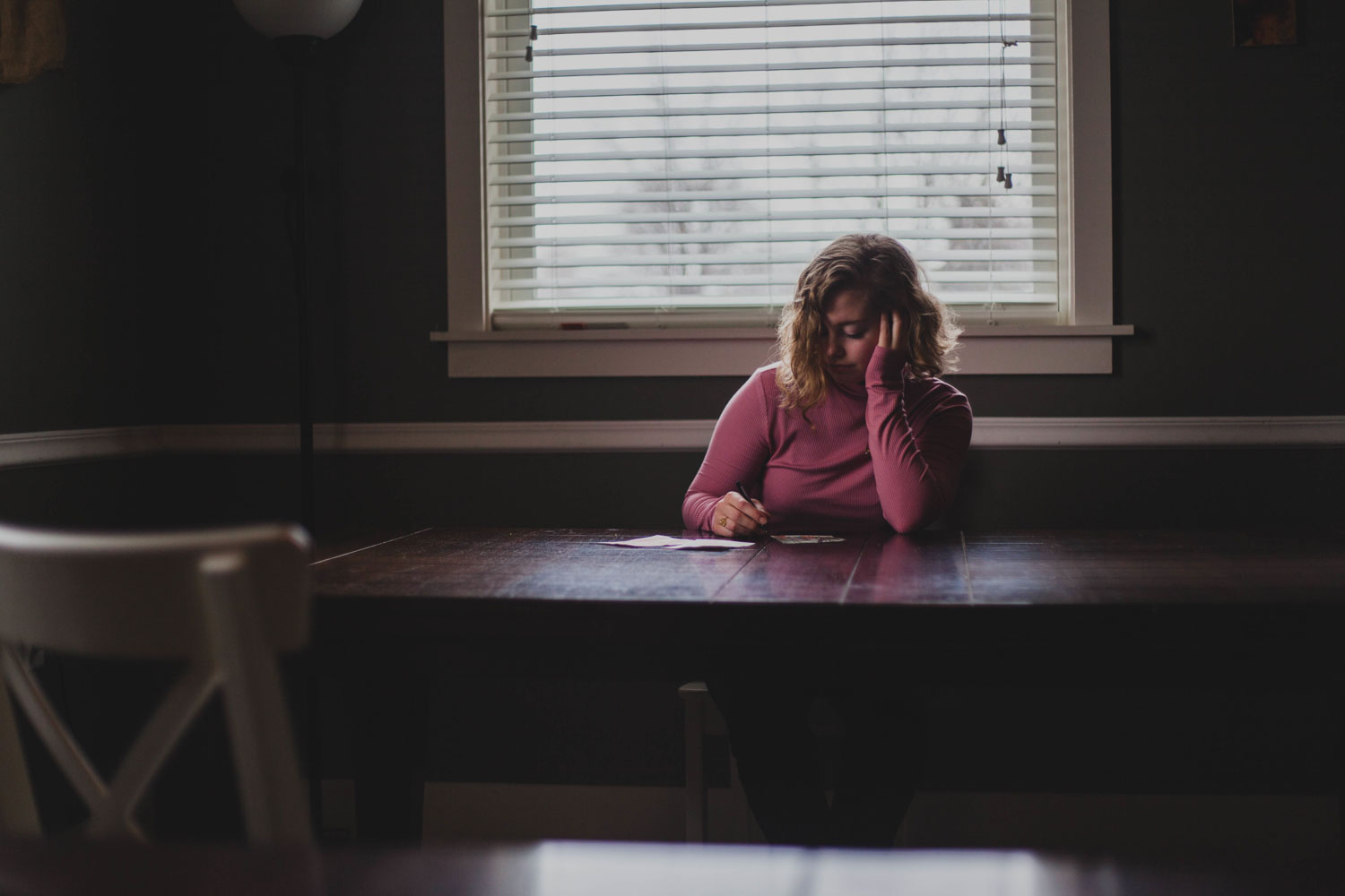 A woman sits at a desk in an office - she looks stressed and confused, her face in her hand as she slumps over.